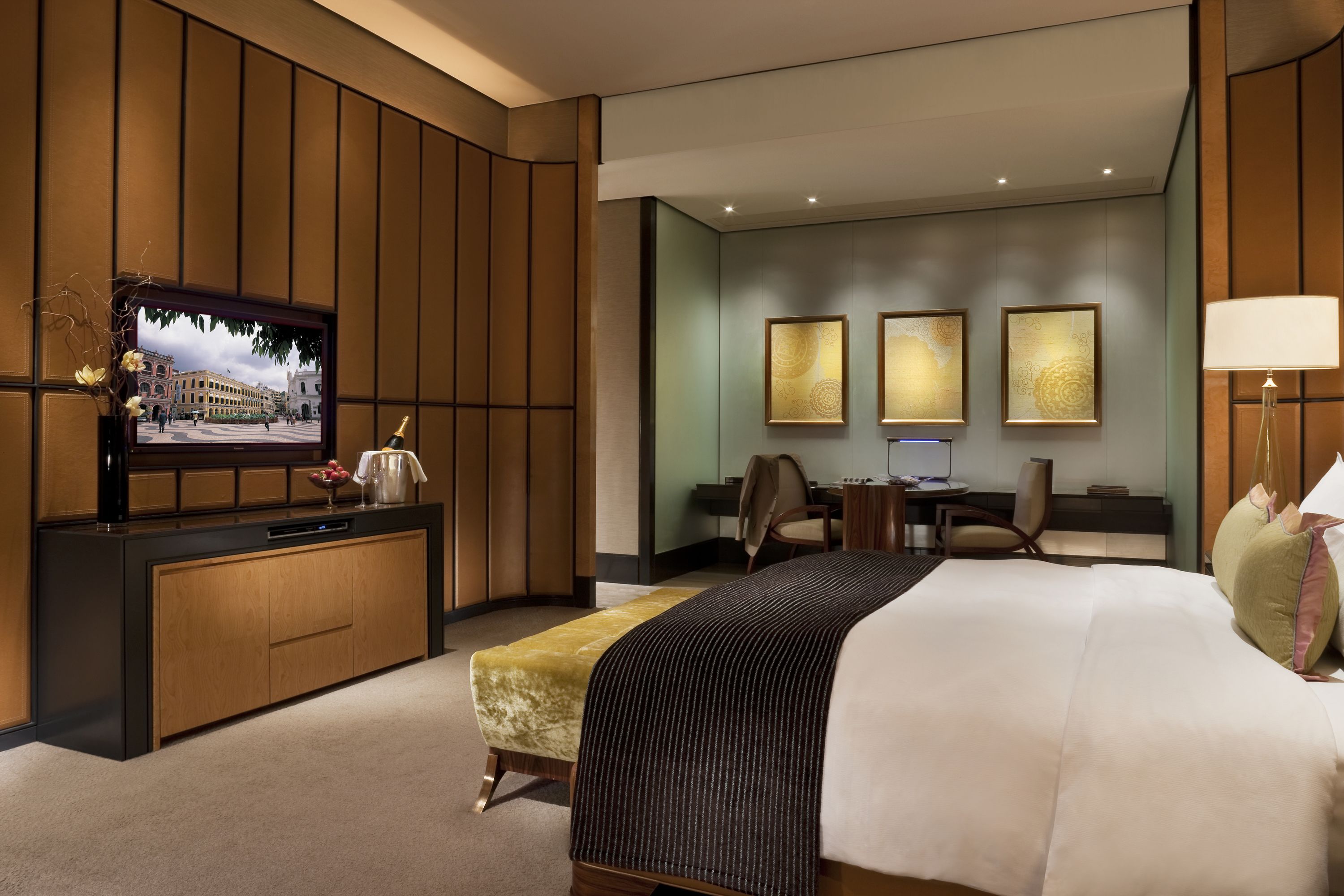 A hotel room with a large bed, a desk, a chair, a television, and artwork on the wall.