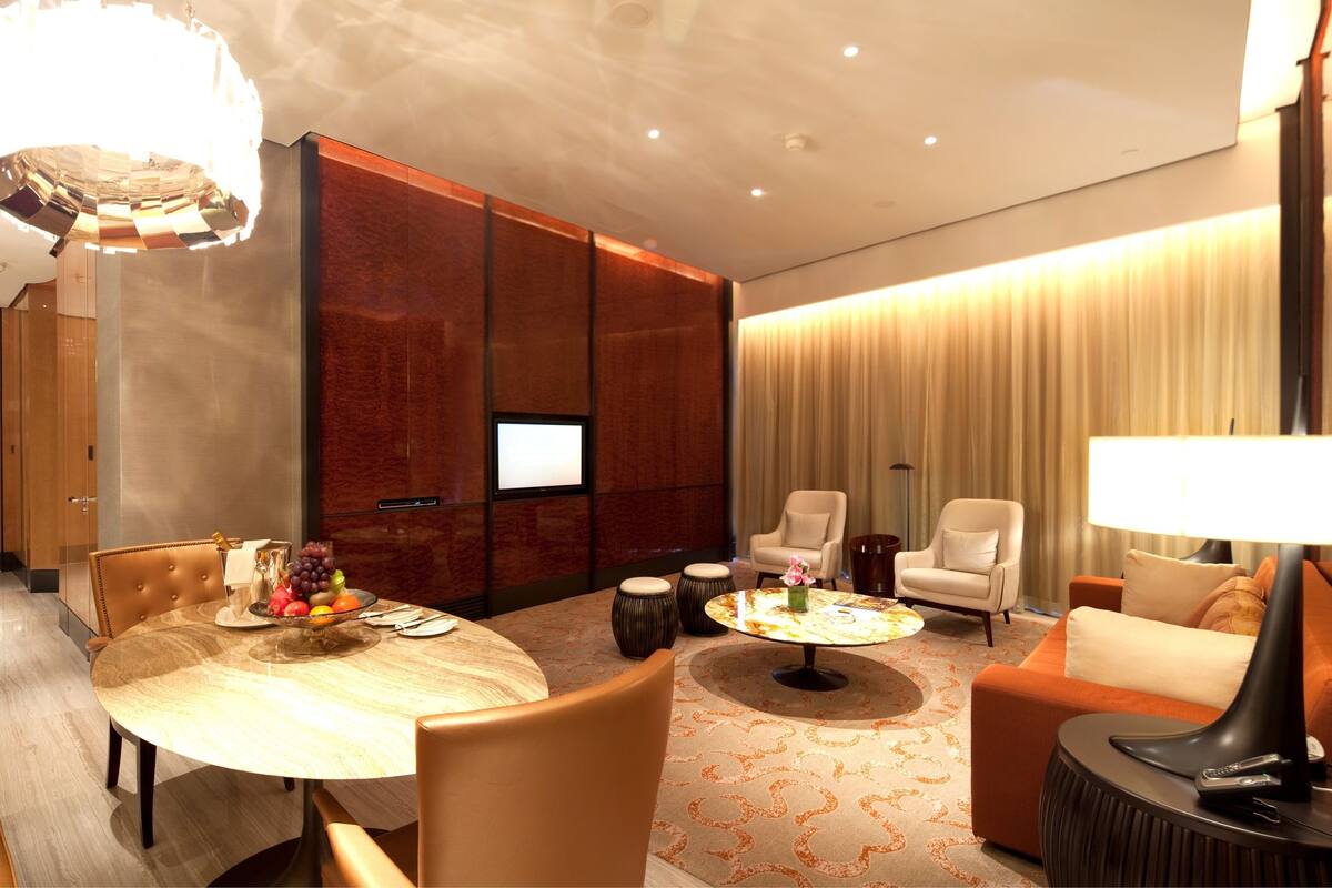 A modern hotel room with a dining area, a sofa, a TV, and a lamp.