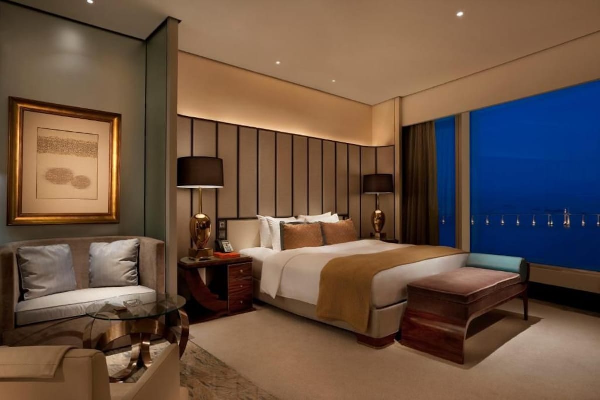 A modern hotel room with a large bed, a sofa, a desk, and a view of the cityscape.