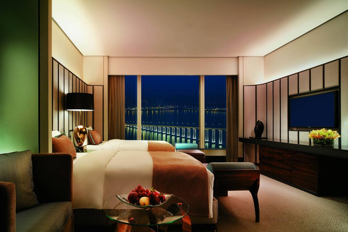 A modern hotel room with a large bed, a seating area, a desk, and a TV.