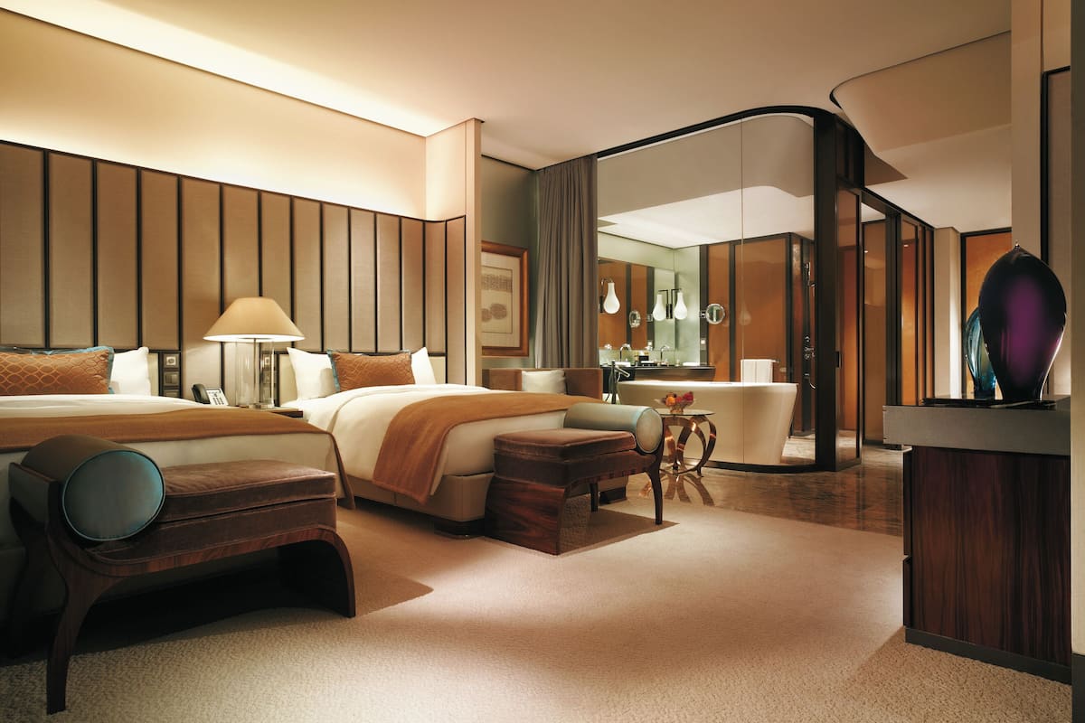 A modern hotel room with a large bed, bedside tables, a desk, and a bathroom with a mirror and sink.