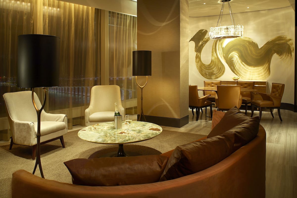 A modern hotel lobby with a seating area, a chandelier, and a large window with a view of the city.