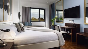 Una habitación de hotel moderna con una cama grande, un escritorio, una silla, un televisor y un ventanal con cortinas.