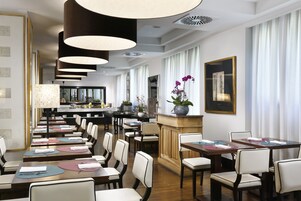 A spacious dining area with multiple tables and chairs, a central bar area, and a view of the kitchen in the background.