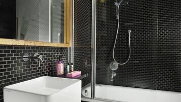 Ein Badezimmer mit einem weißen Waschbecken, einer Duschkabine aus Glas und einem Spiegel mit Holzrahmen.