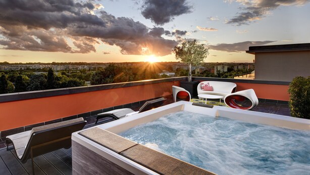 Terraza en la azotea con jacuzzi, mobiliario exterior y vista a la ciudad al atardecer.