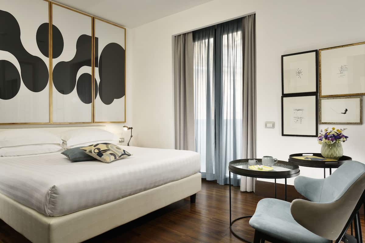 A hotel room with a large bed, a small table with a vase, and a chair.