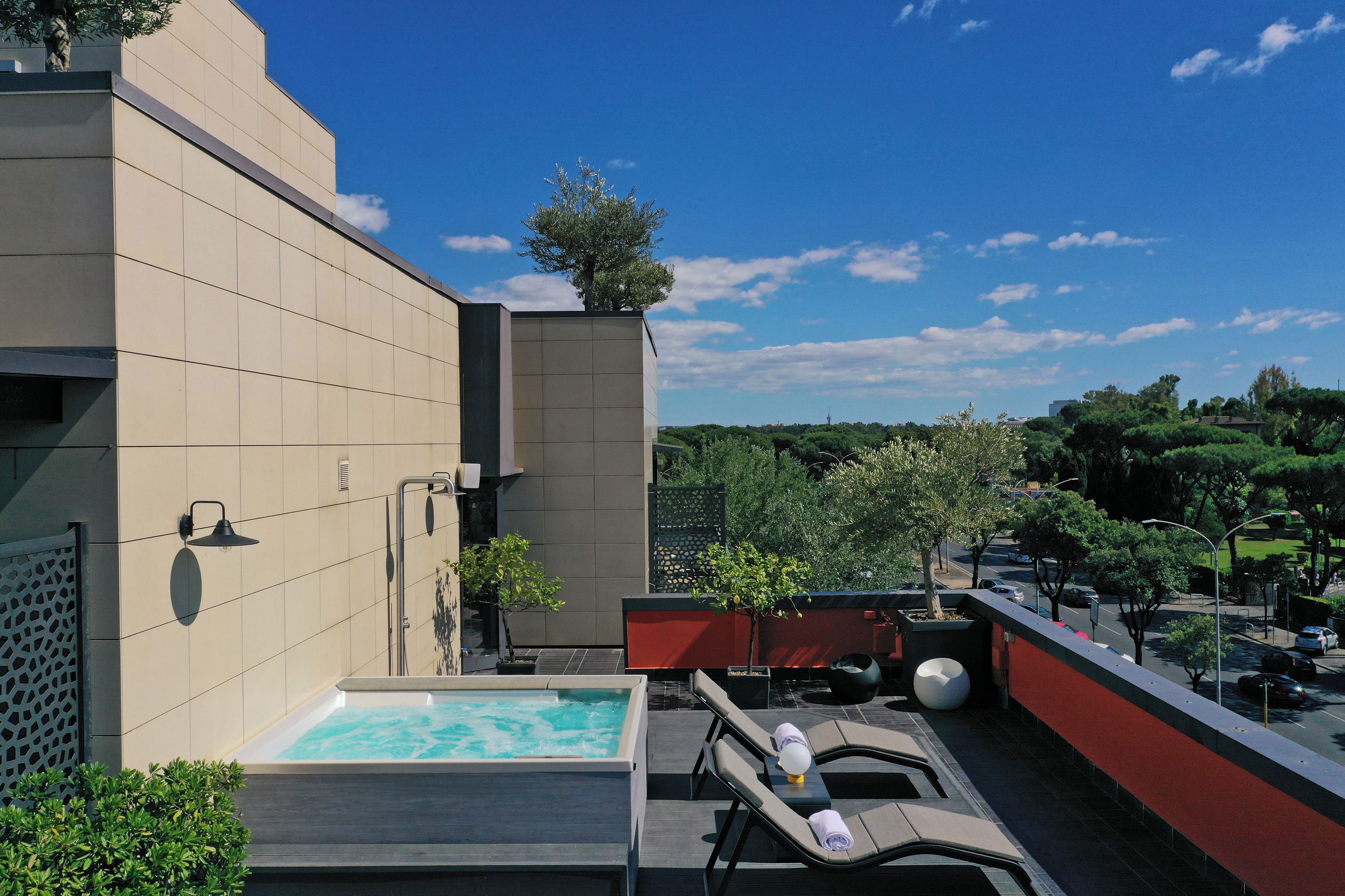Area piscina sul tetto con vista chiara sullo skyline cittadino, facciata di un edificio moderno e giardino curato.