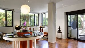 Un interior moderno con una mesa de vidrio central, una computadora portátil, un jarrón con flores y un gran ventanal con vistas a zonas verdes.