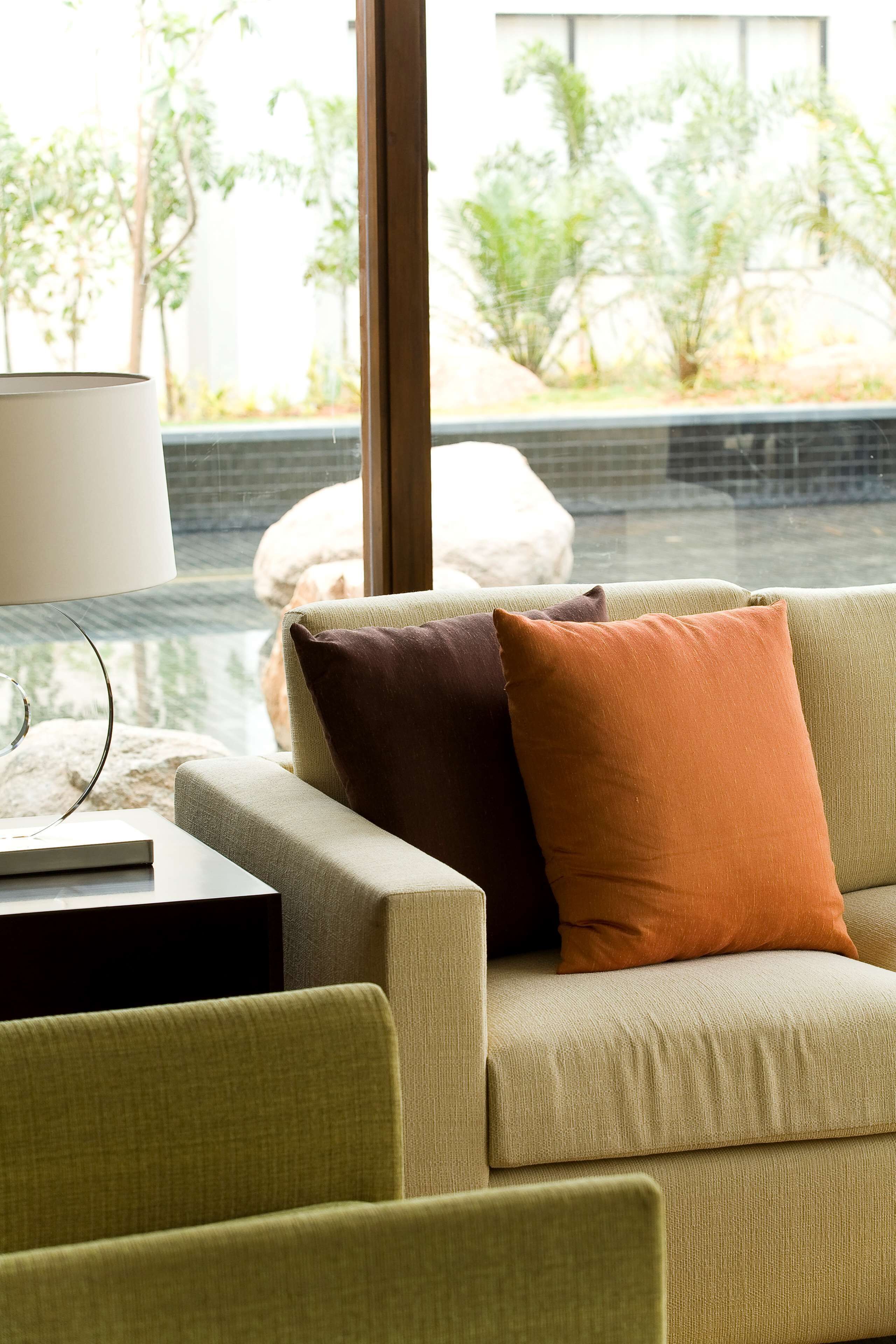 A modern living room with a sofa and cushions, a glass coffee table, and a view of an outdoor garden through large windows.