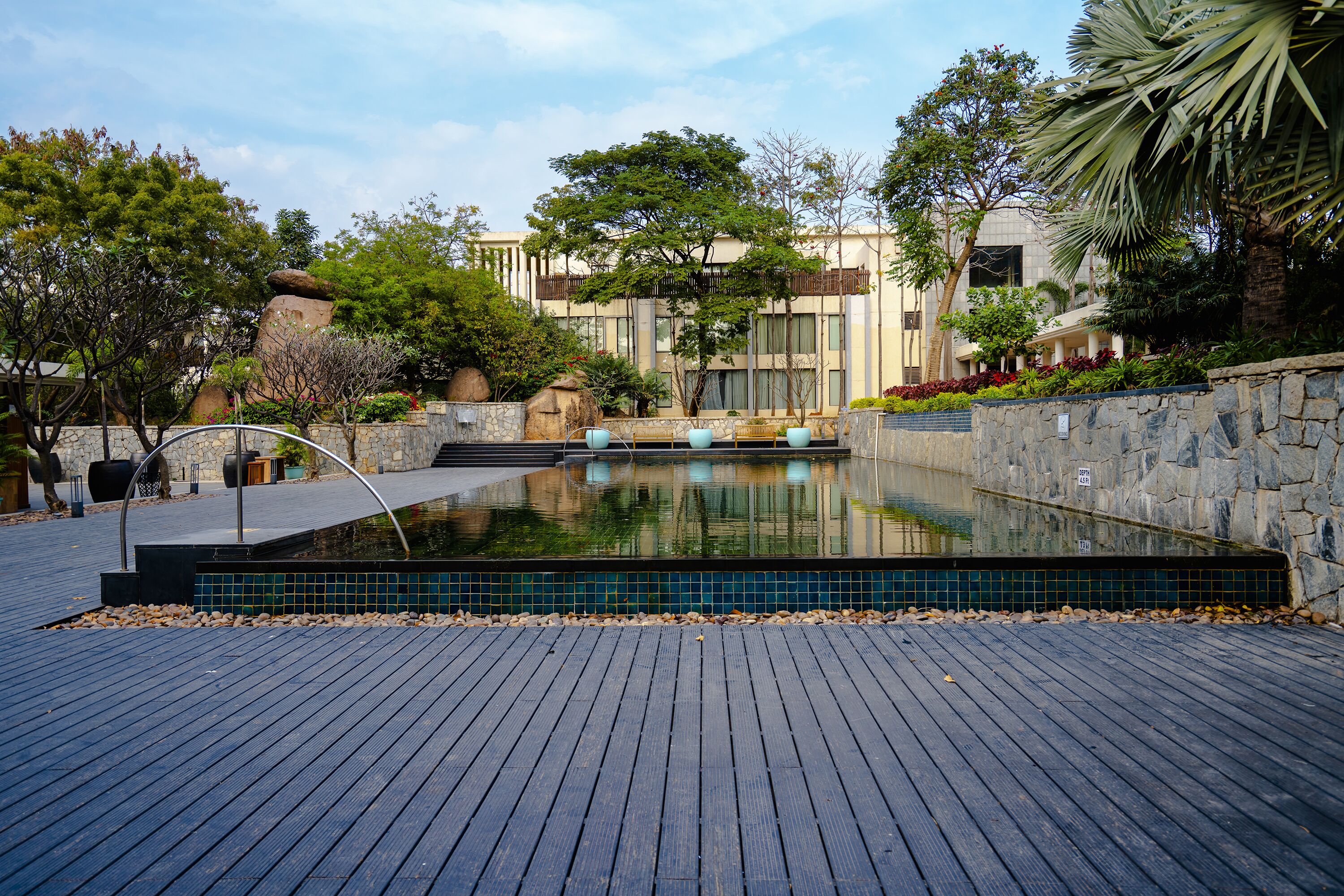 A swimming pool with a stone border, surrounded by a wooden deck and various plants.