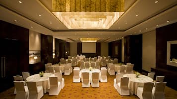 A banquet hall with round tables and chairs, a large chandelier, and a carpeted floor.