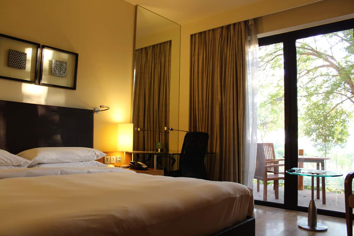 A hotel room with a large bed, a desk with a lamp, a chair, and a view of the outdoors through a sliding glass door.