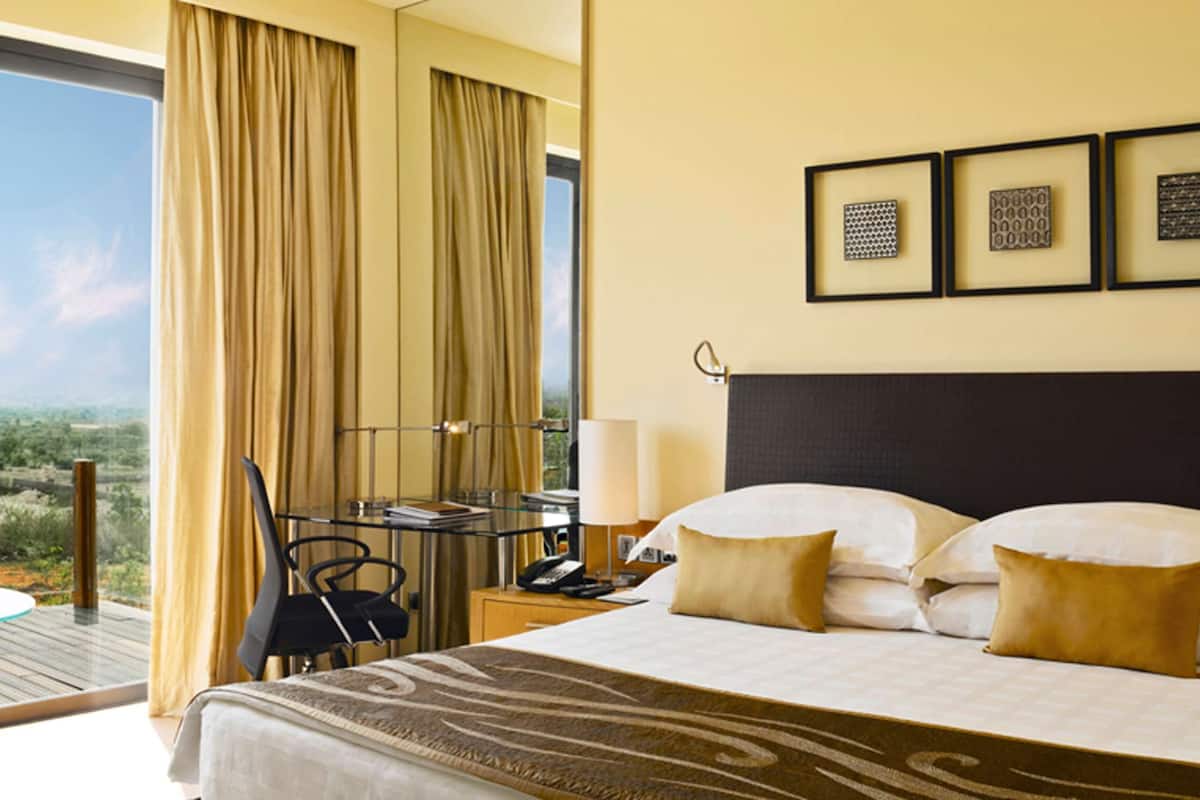 A hotel room with a large bed, a desk, a chair, and a view of the landscape.