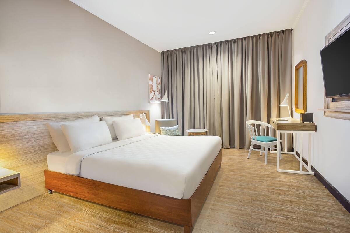 Une chambre d’hôtel avec un grand lit, un bureau, une chaise, une lampe et un téléviseur.