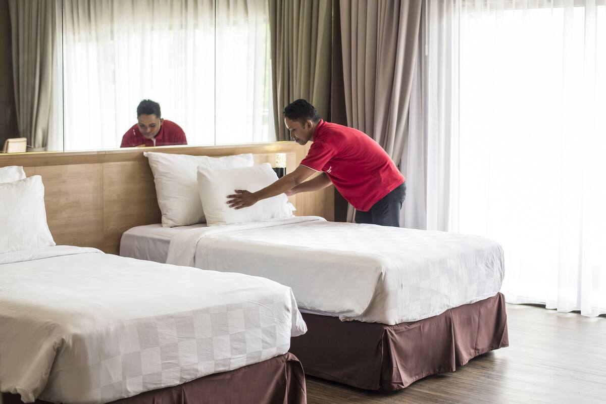 Une chambre d’hôtel avec deux lits, une tête de lit en bois et une grande fenêtre avec des rideaux.