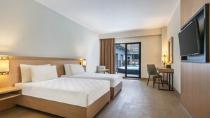 Ein Hotelzimmer mit zwei Betten, einem Schreibtisch, einem Sessel und einem Fernseher, mit Blick ins Freie.