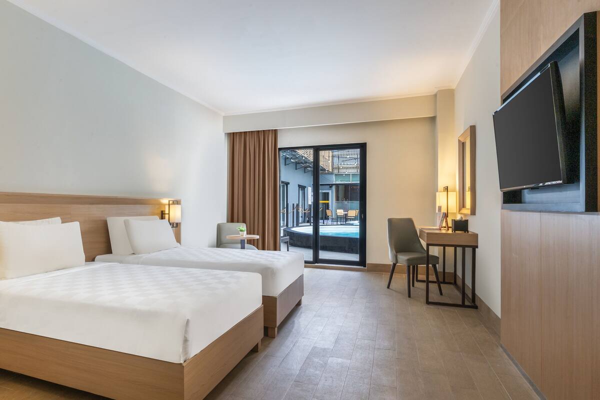Une chambre d’hôtel avec deux lits, un bureau, une chaise, une télévision et une vue sur l’espace extérieur.
