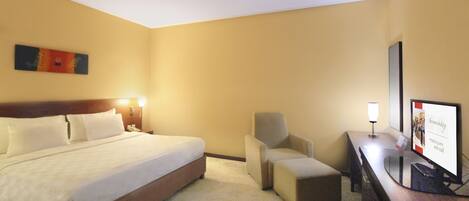 A hotel room with a bed, a chair, a desk with a computer, and a television.