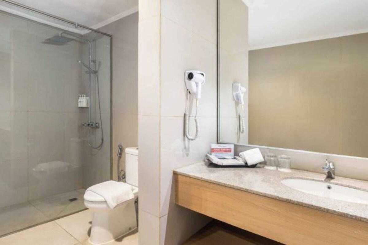 A hotel bathroom with a glass-enclosed shower, a toilet, a sink with a vanity, and a large mirror.