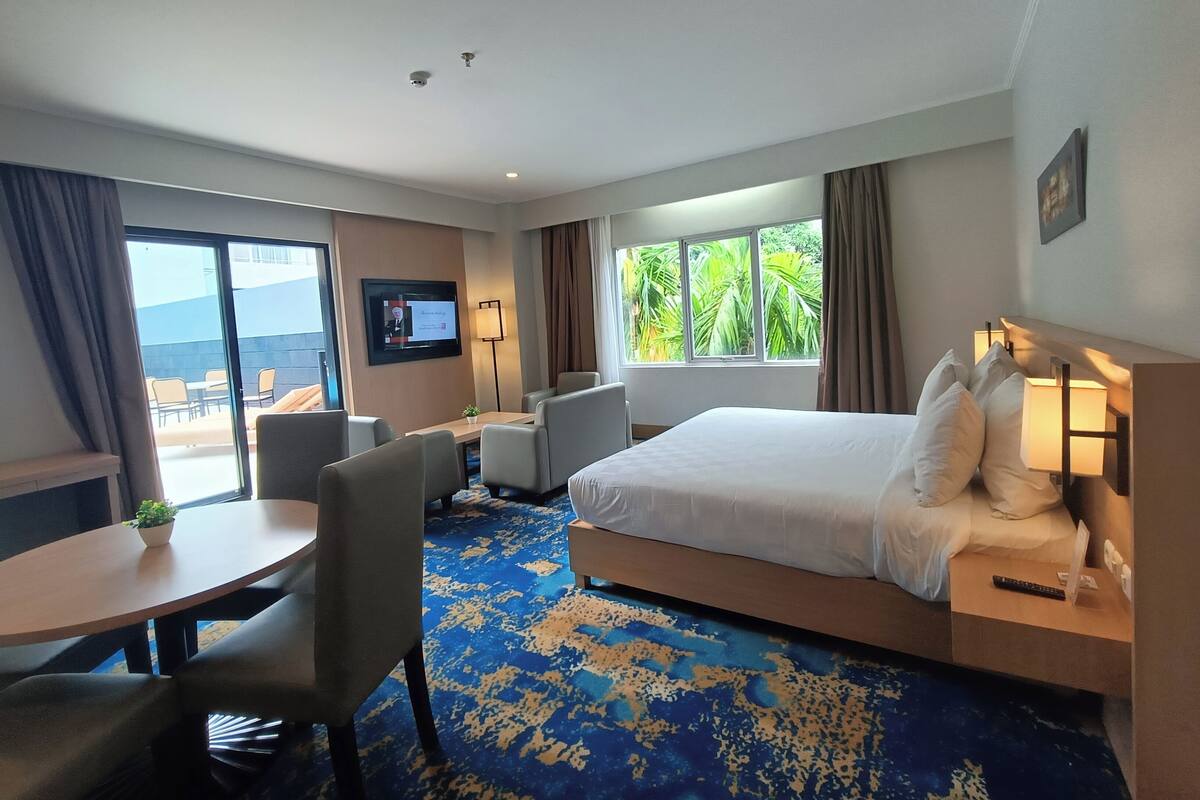 Une chambre d’hôtel équipée d’un lit, d’un bureau, d’une chaise, d’une télévision et d’une fenêtre donnant sur un paysage verdoyant.