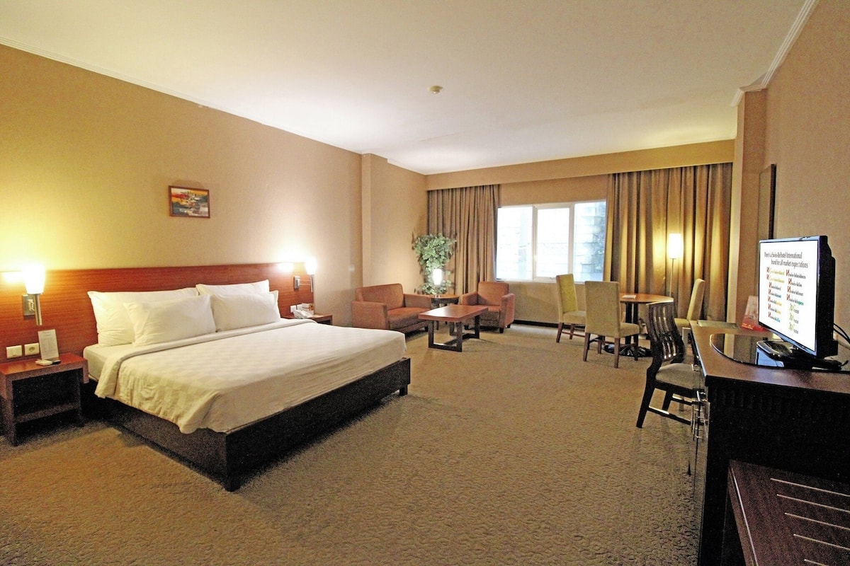 Une chambre d’hôtel avec un grand lit, un bureau avec un ordinateur, une chaise, une petite table et un téléviseur.
