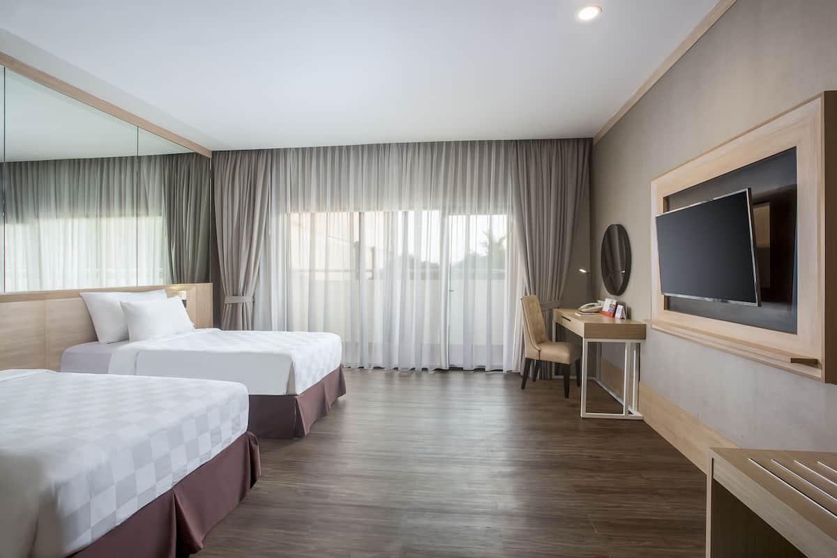Une chambre d’hôtel avec deux lits, un bureau, une télévision et une grande fenêtre avec des rideaux.