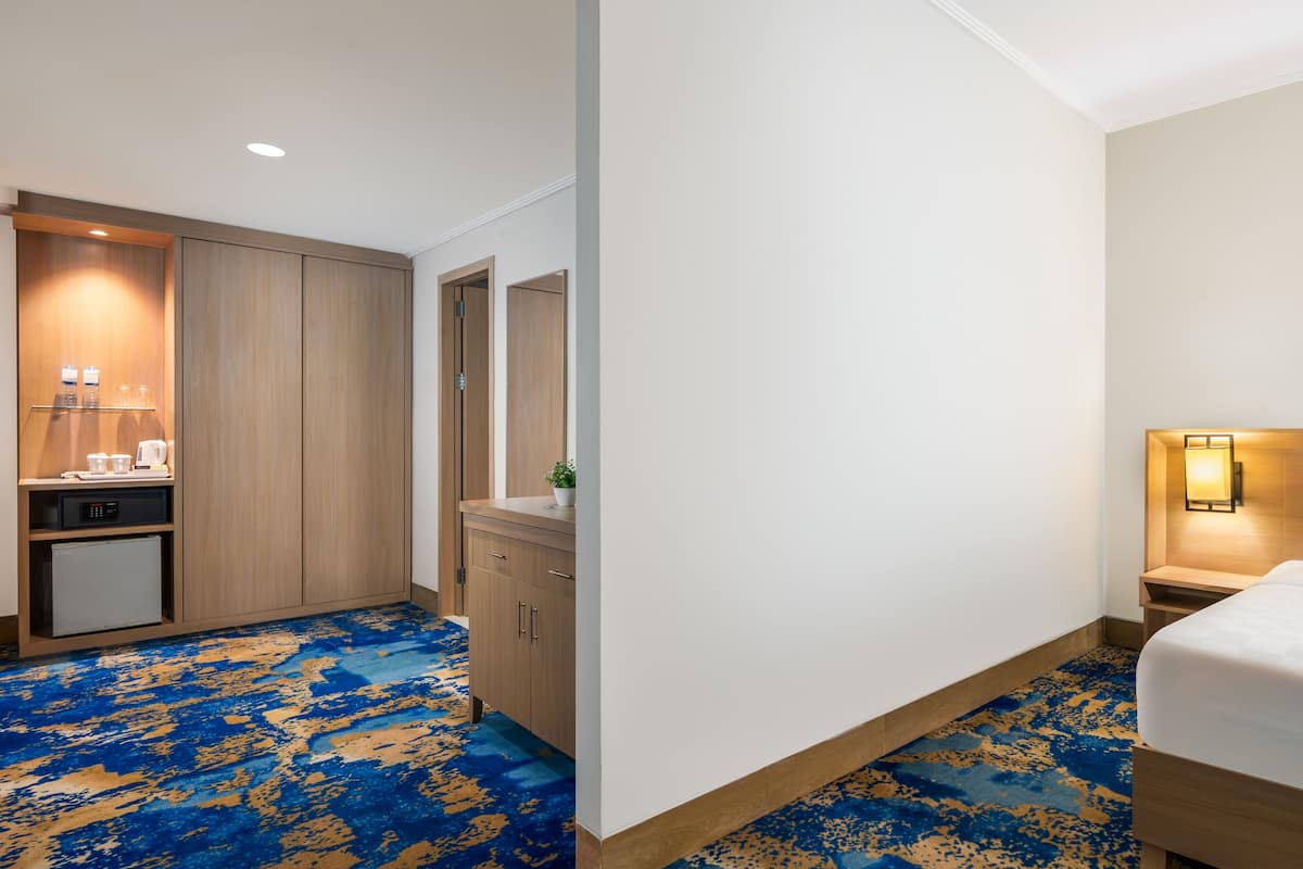 Une chambre d’hôtel comprenant un lit, un bureau avec un ordinateur, un petit réfrigérateur, un miroir et une salle de bain.