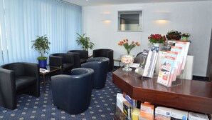 Un hall d’hôtel avec des fauteuils en cuir noir, un comptoir d’accueil où sont disposées des brochures et des plantes en pot.