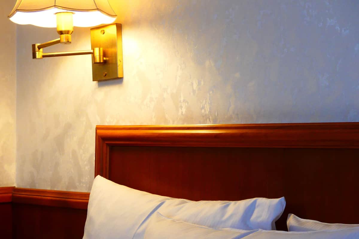 Ein Hotelzimmer mit einem Holzkopfteil, einer Wandleuchte und einem ordentlich bezogenen Bett mit weißen Laken.