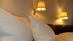 Un lit bien fait, avec des oreillers blancs et deux lampes fixées au mur, diffusant une lumière douce.