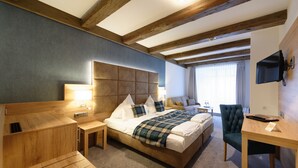 Une chambre d’hôtel avec un grand lit, un bureau en bois, une chaise, une télévision et une fenêtre avec des rideaux.