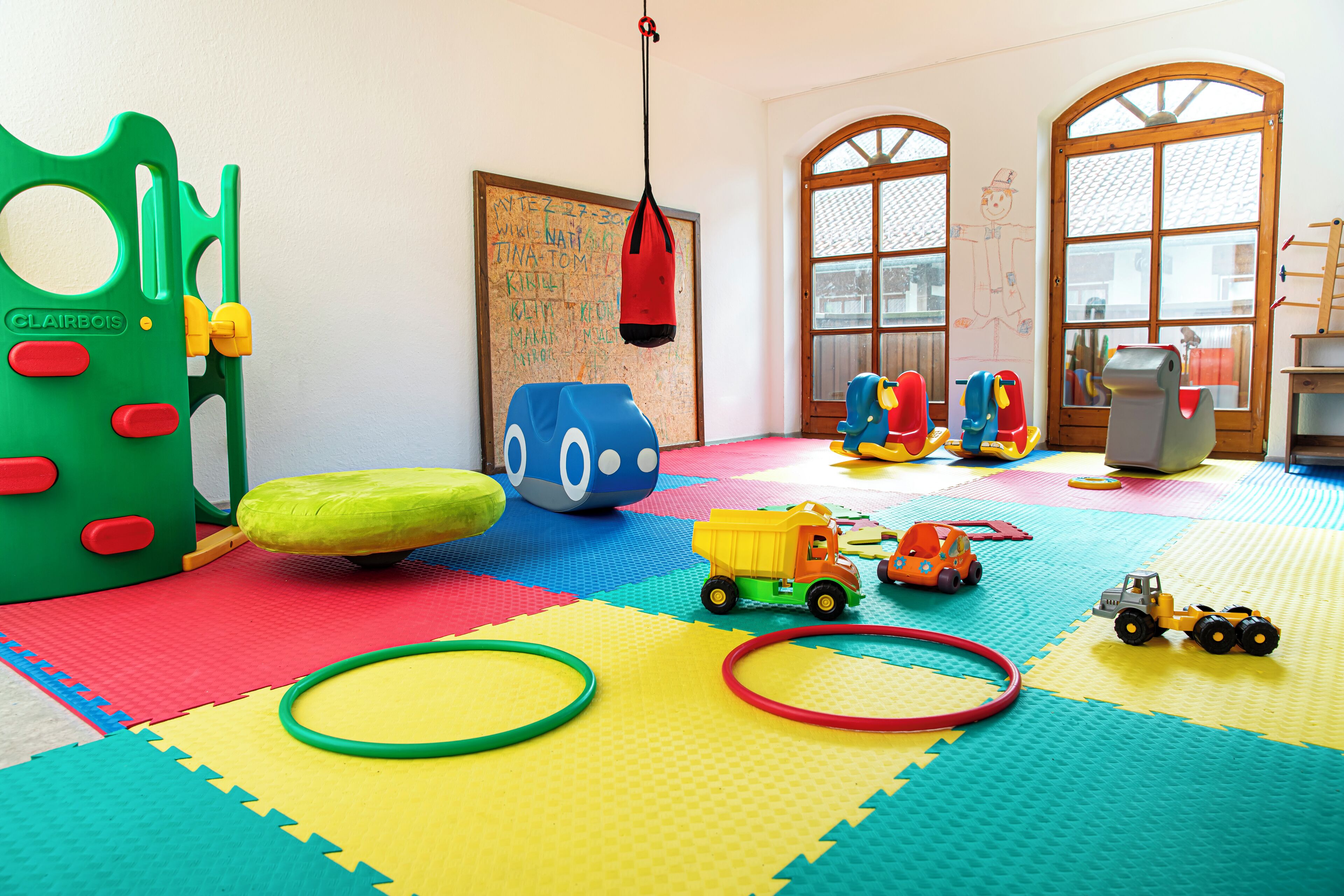 A playroom with colorful foam mats, a green play structure, and various toys.
