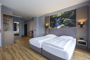 A modern hotel room with a large bed, a bathroom with a mirror, and a wall-mounted TV displaying a nature scene. - Hotel am Badepark Waldkirchen (Waldkirchen)