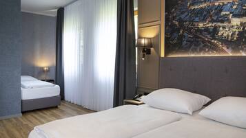A hotel room with a bed, a nightstand, a lamp, and a large window with curtains.