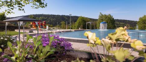 Una piscina con una fuente, rodeada por un jardín con flores moradas y un pabellón.