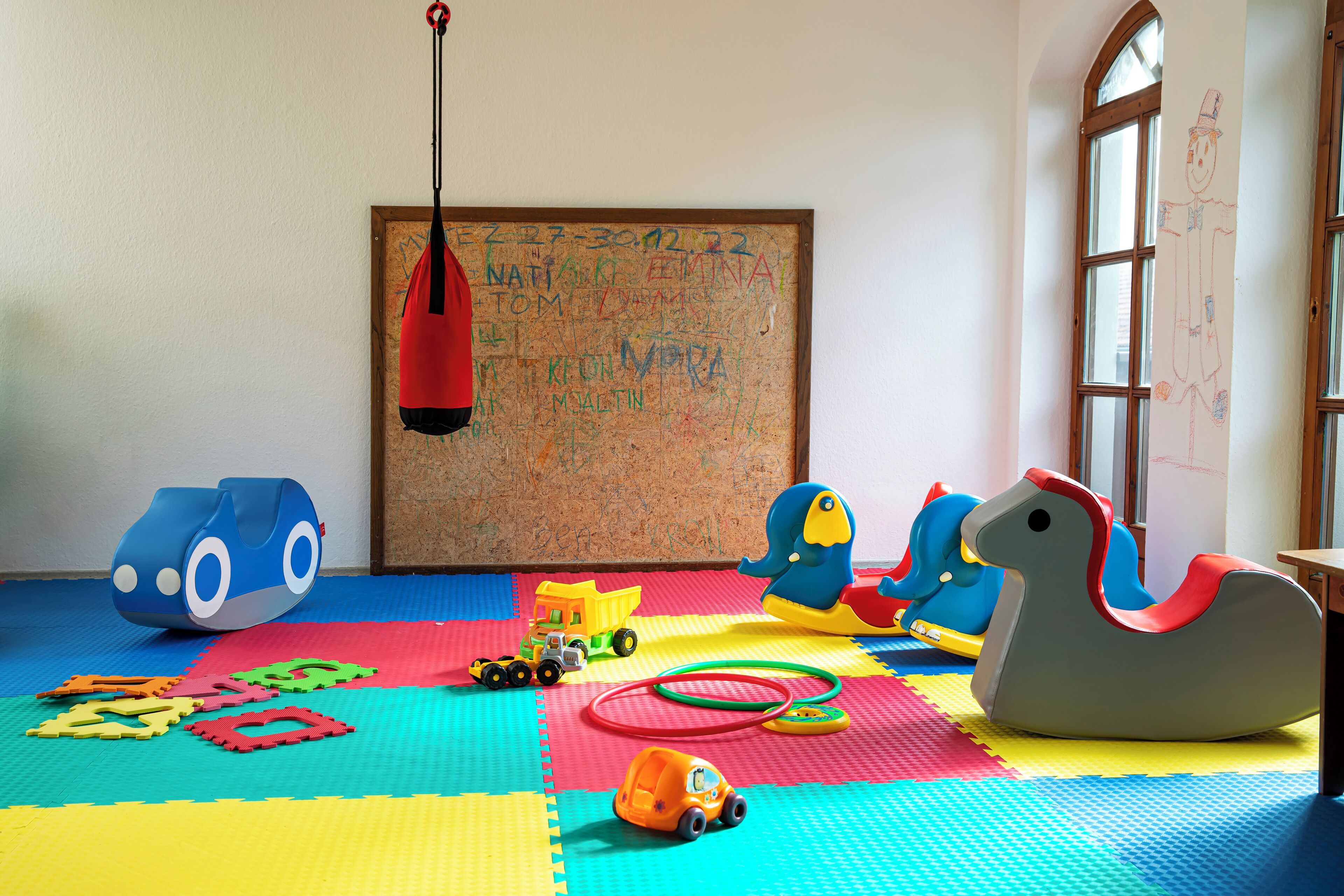 Un cuarto de juegos con alfombras de espuma coloridas, una pizarra y distintos juguetes.