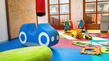 Zona de juegos con colchonetas de espuma, una estructura azul y verde, y un camión de juguete.