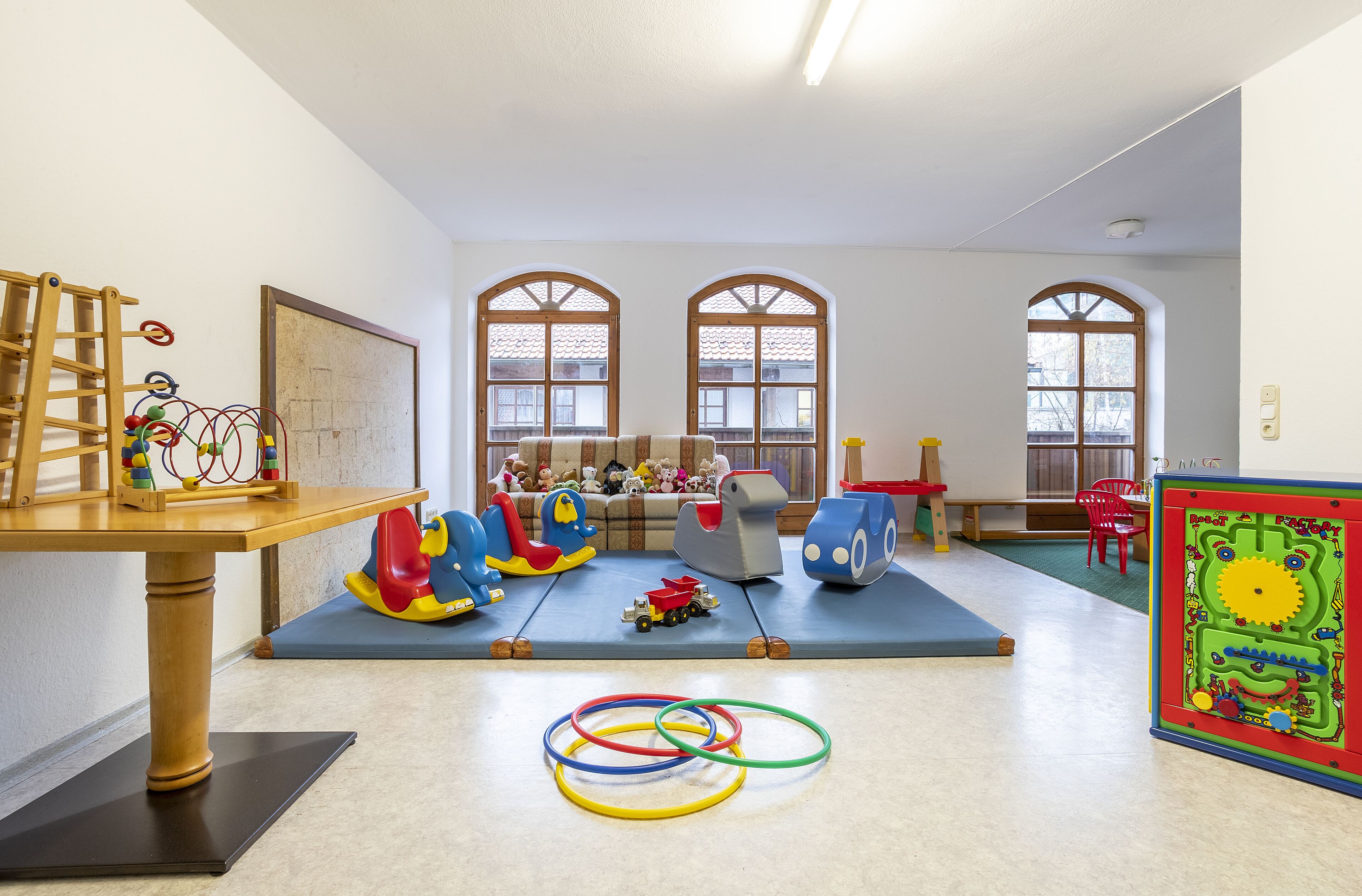 Una sala de juegos con una mesa de madera, juguetes de colores y un tapete en el suelo.
