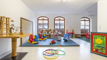 Ein Spielzimmer mit einem Holztisch, bunten Spielsachen und einer Matte auf dem Boden.