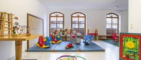 A playroom with a wooden table, colorful toys, and a mat on the floor.