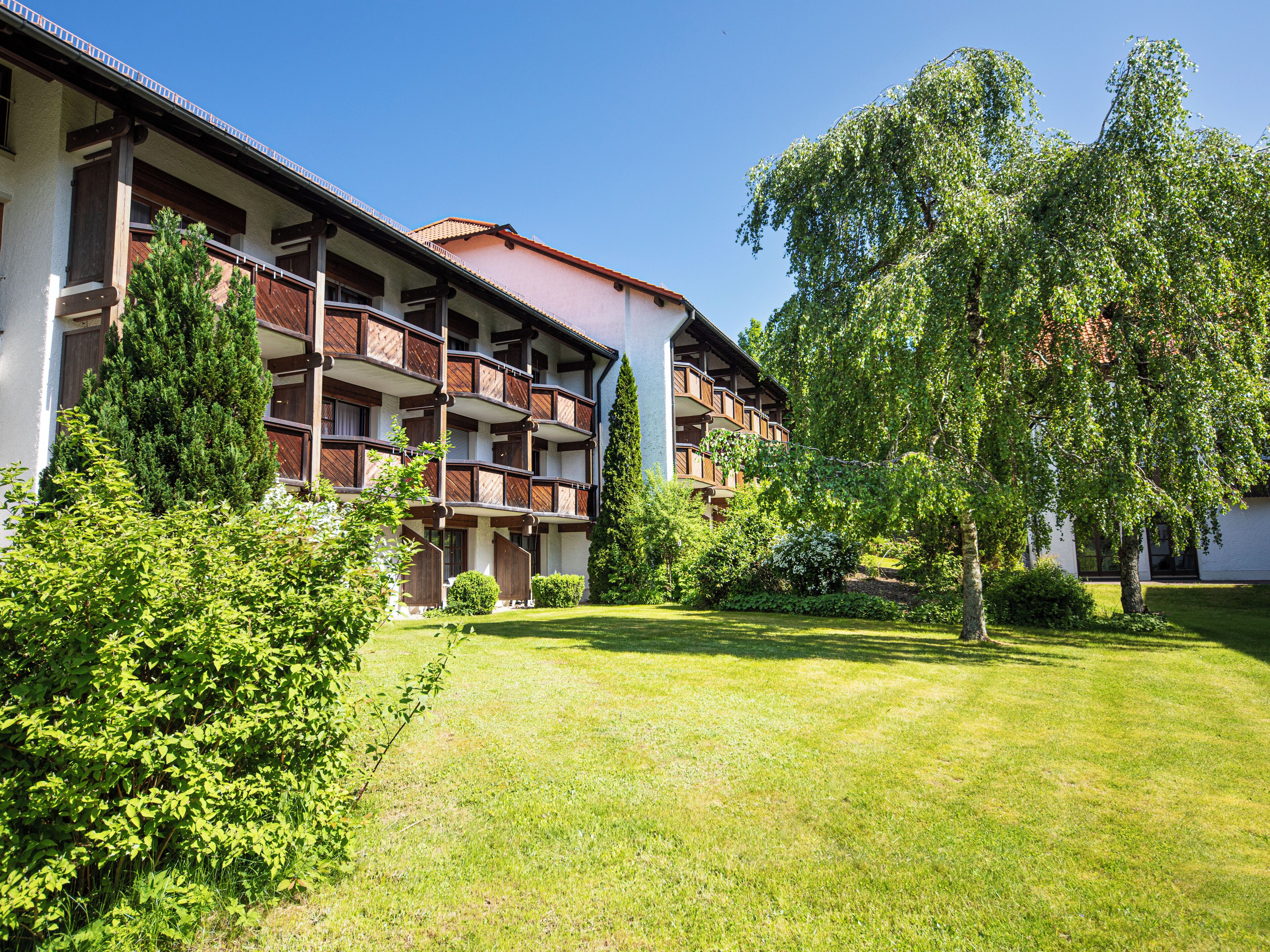 A multi-story hotel with balconies, surrounded by well-maintained lawns and trees.