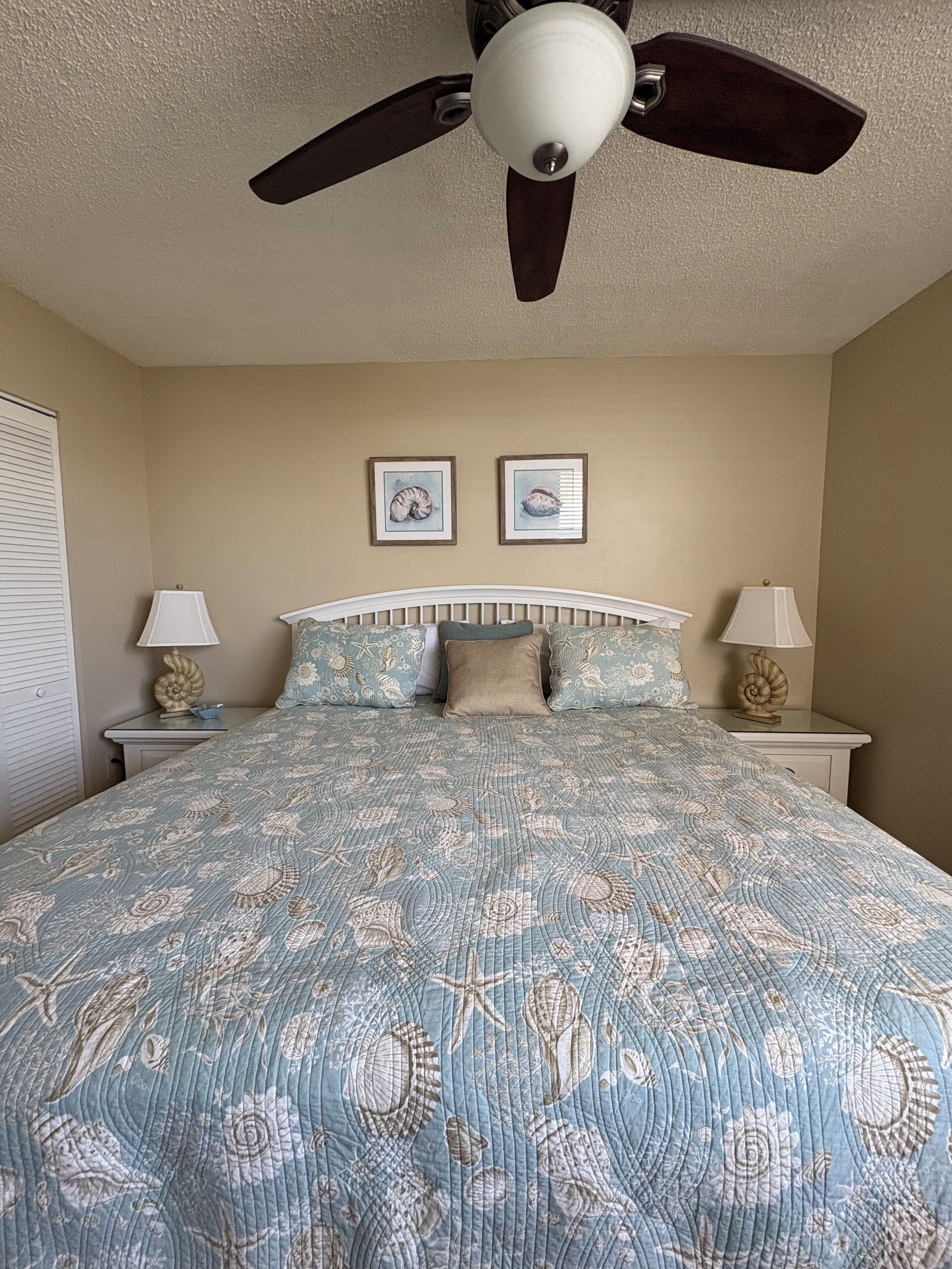 A bedroom with a large bed, two nightstands, a ceiling fan, and two framed pictures on the wall.
