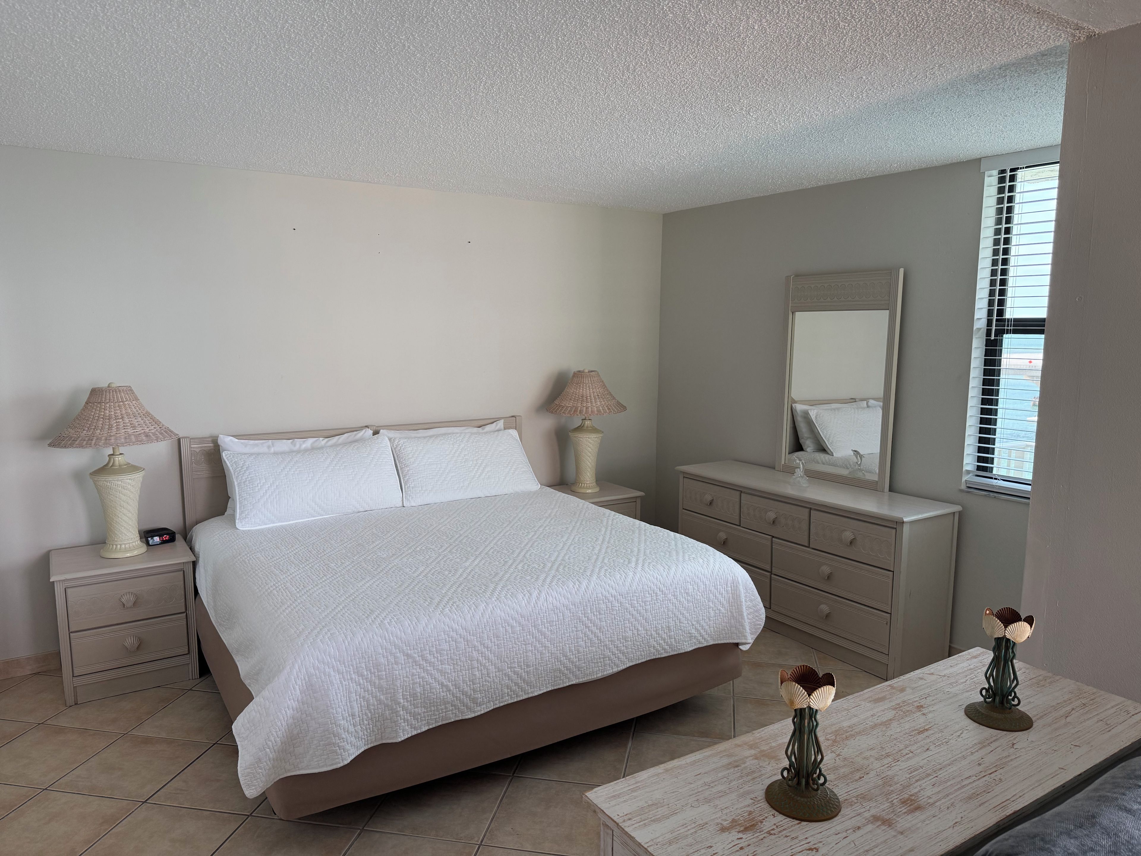 A bedroom with a bed, bedside tables, a dresser, a mirror, and a window.