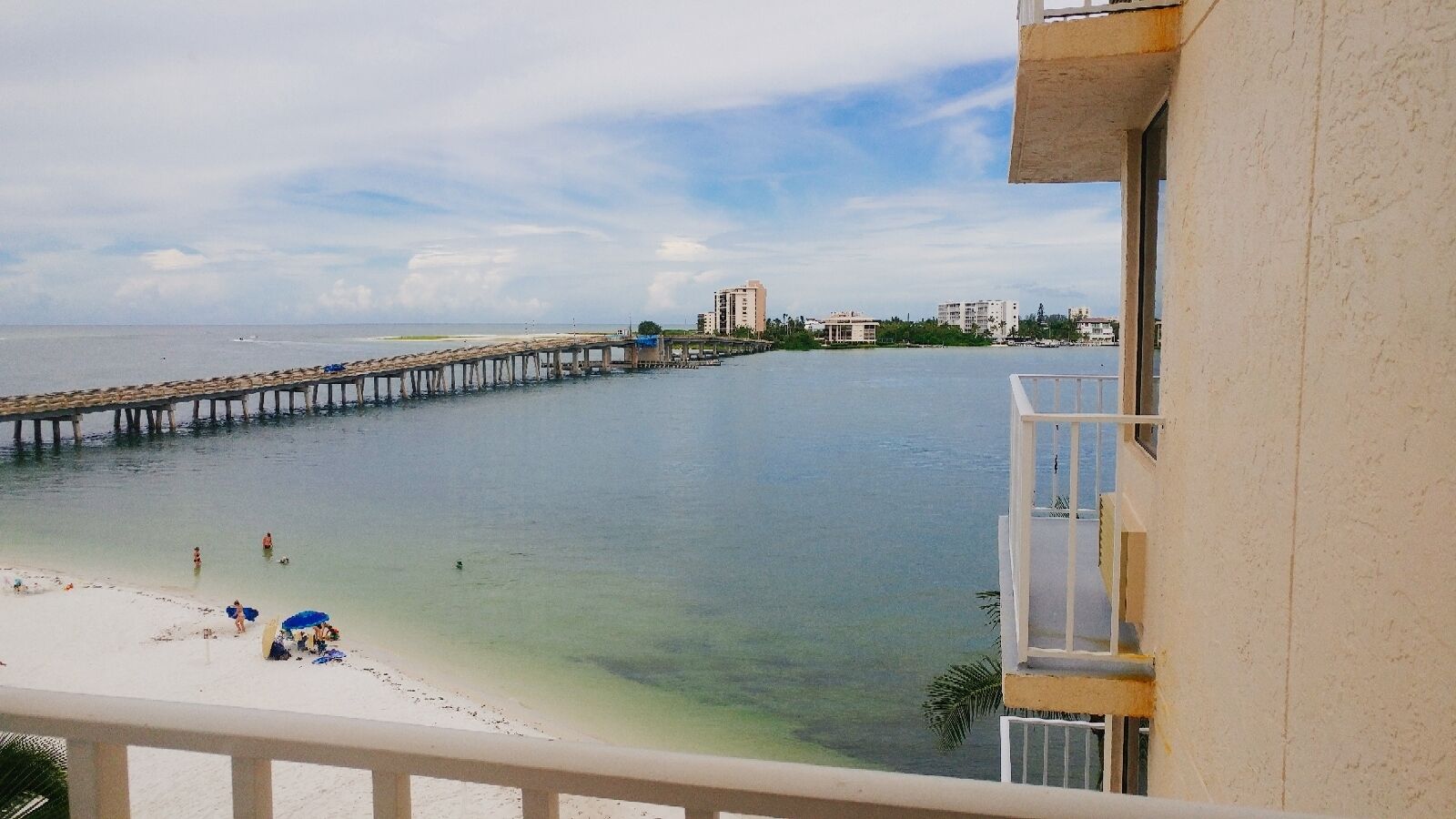A beach with a pier extending into the water, a few people on the shore, and buildings in the background.