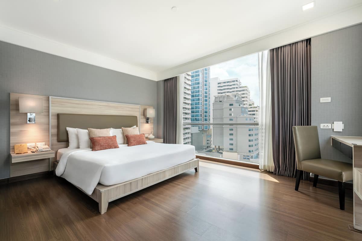 A modern hotel room with a large bed, a desk, and a view of the cityscape.