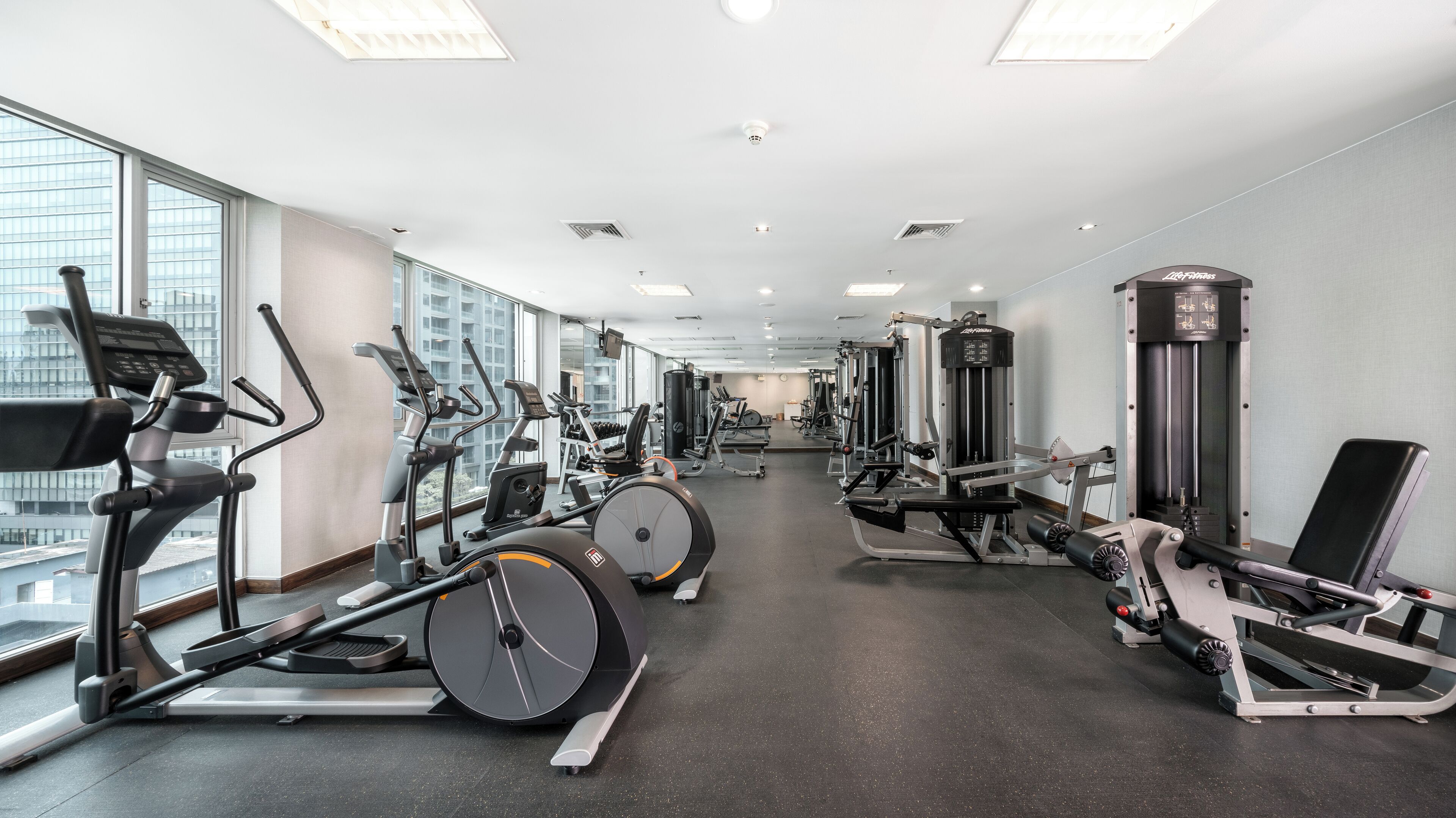 Ein modernes Fitnessstudio mit verschiedenen Trainingsgeräten, großen Fenstern und Blick auf die Stadt.