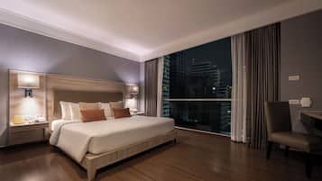 A modern hotel room with a large bed, bedside lamps, a desk, and a view of the city at night.