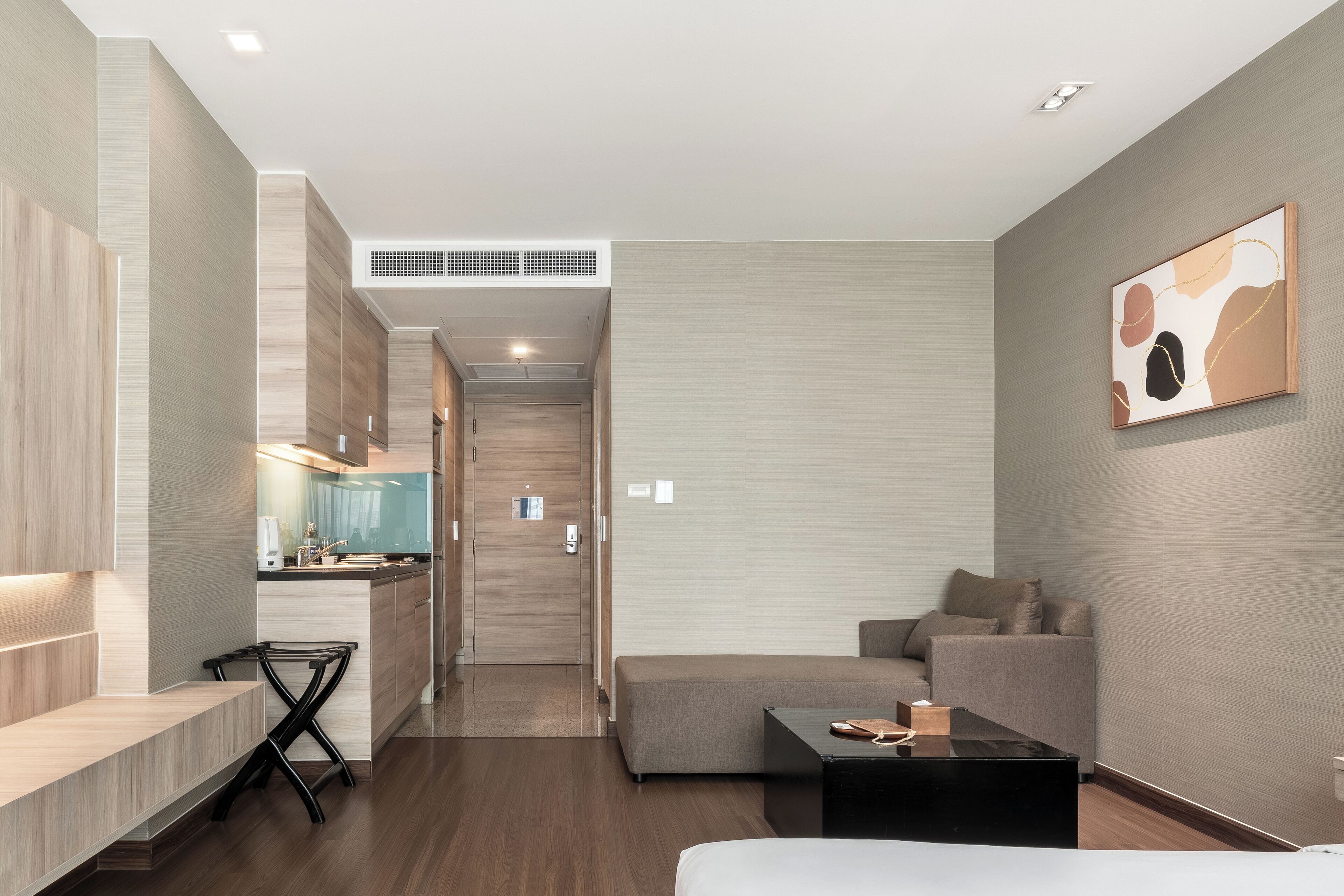 Quarto de hotel moderno com cozinha compacta, sofá, mesa de centro e cama.