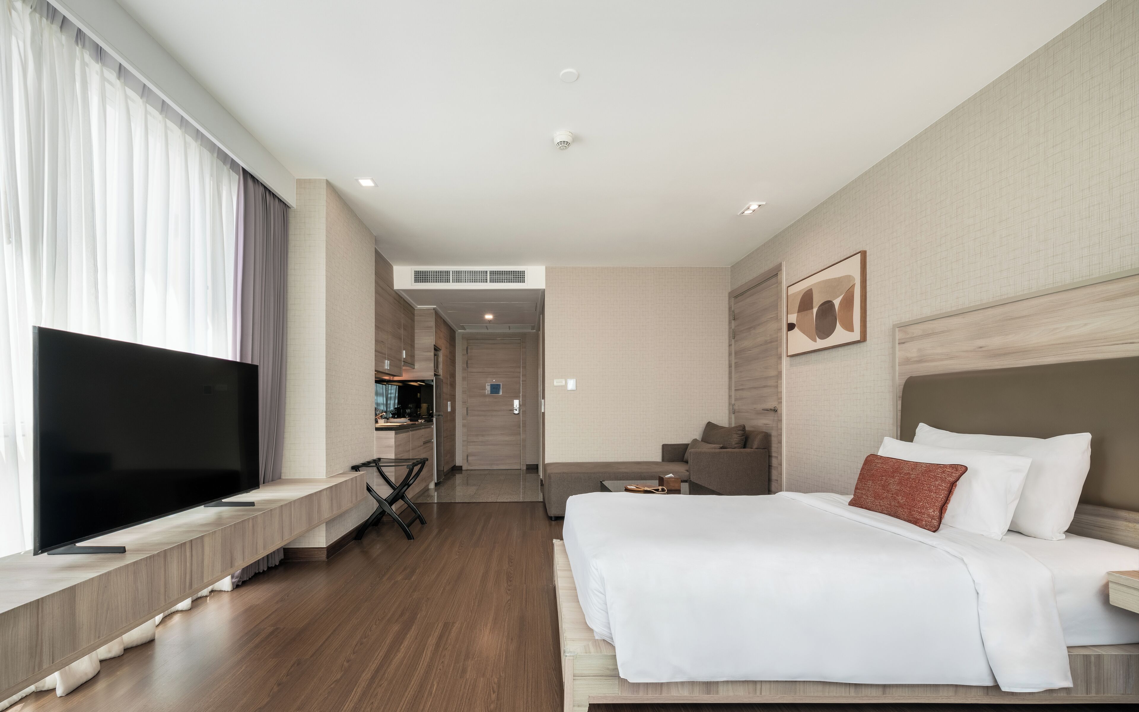 A hotel room with a large bed, a TV, a desk, and a view of the hallway.